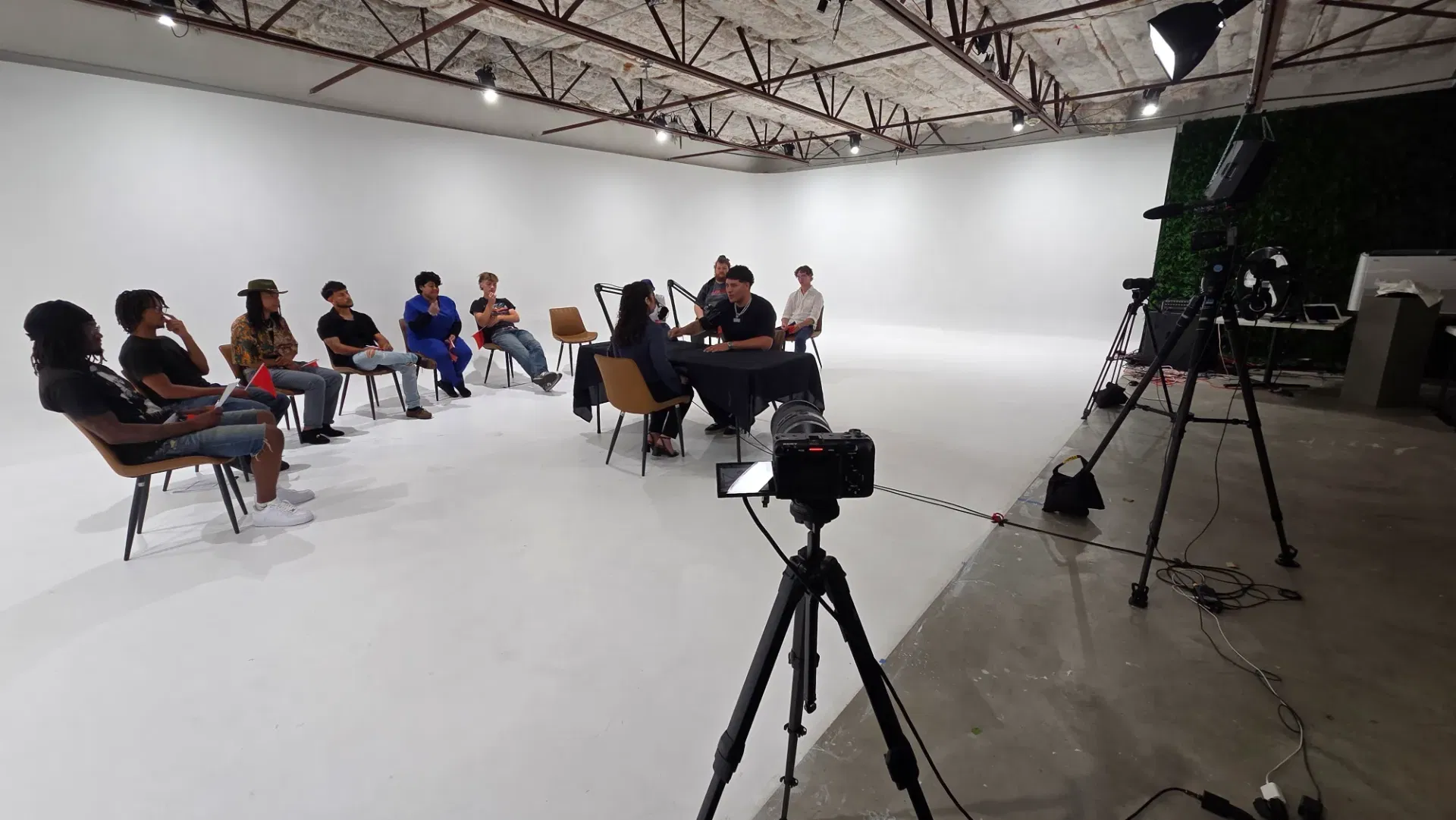 Side profile of the white infinity wall setup, showing cable routing, boom mic placement, and contestant seating along the studio perimeter.