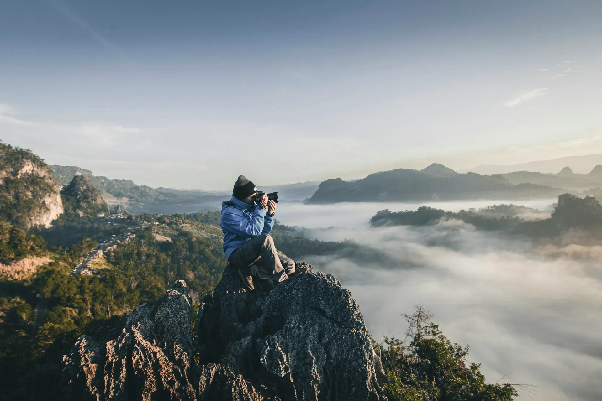 A cinematographer sitting on a mountain summit framing a shot across the landscape.