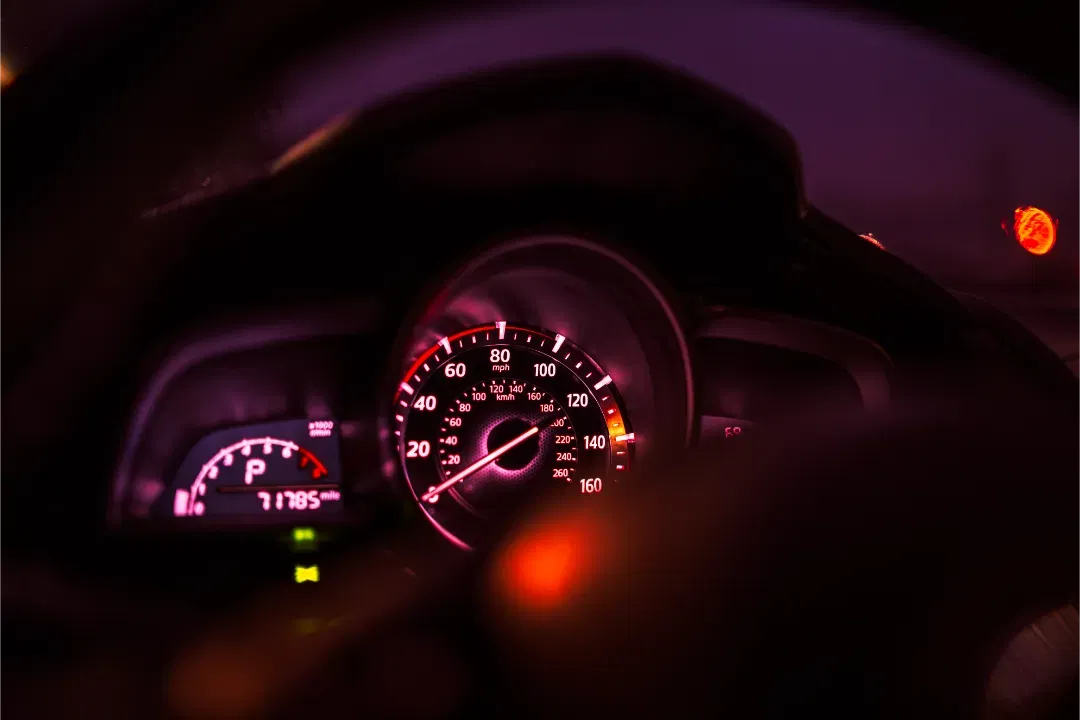 A close-up cinematic shot of a car's speedometer dashboard illuminated with red lights at night.