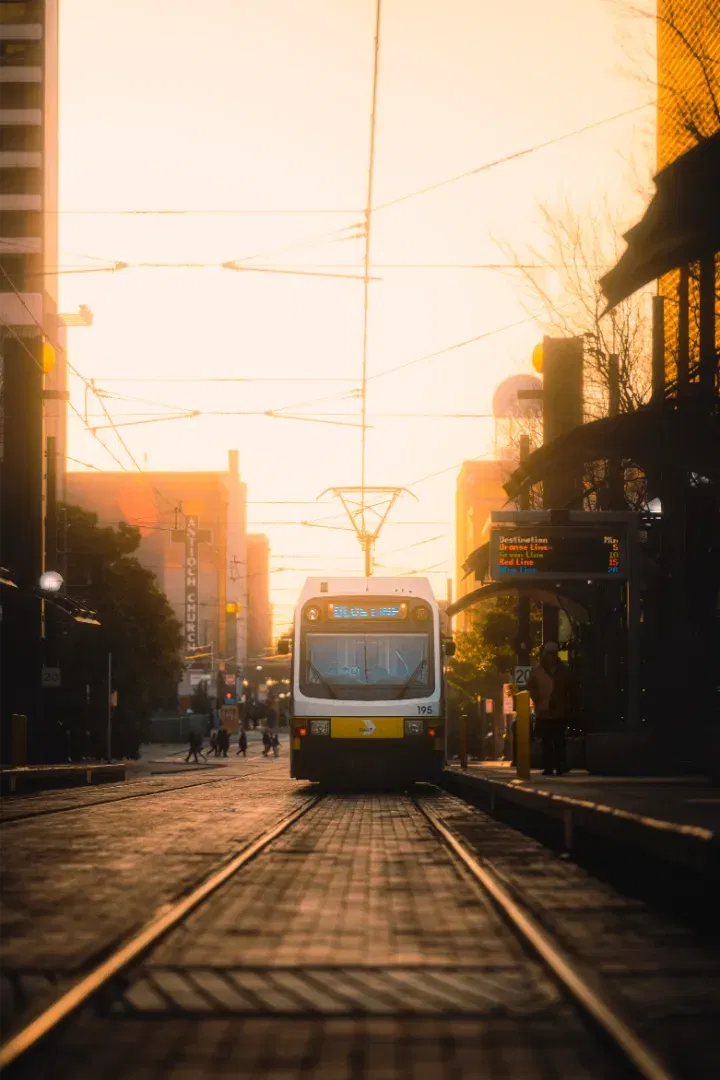 A streetcar approaching a platform at sunset, bathed in a warm golden-orange glow.