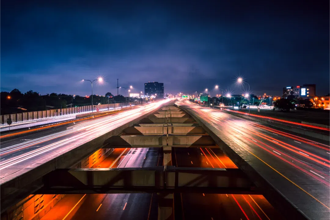 A low perspective of a concrete highway bridge dividing traffic light trails on both sides under a twilight sky.