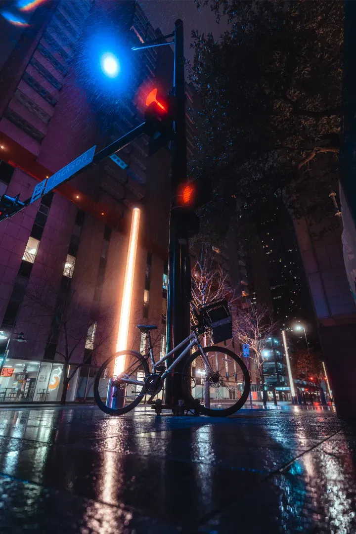 A bicycle parked next to a utility pole on a wet street at night, illuminated by a warm light beam.