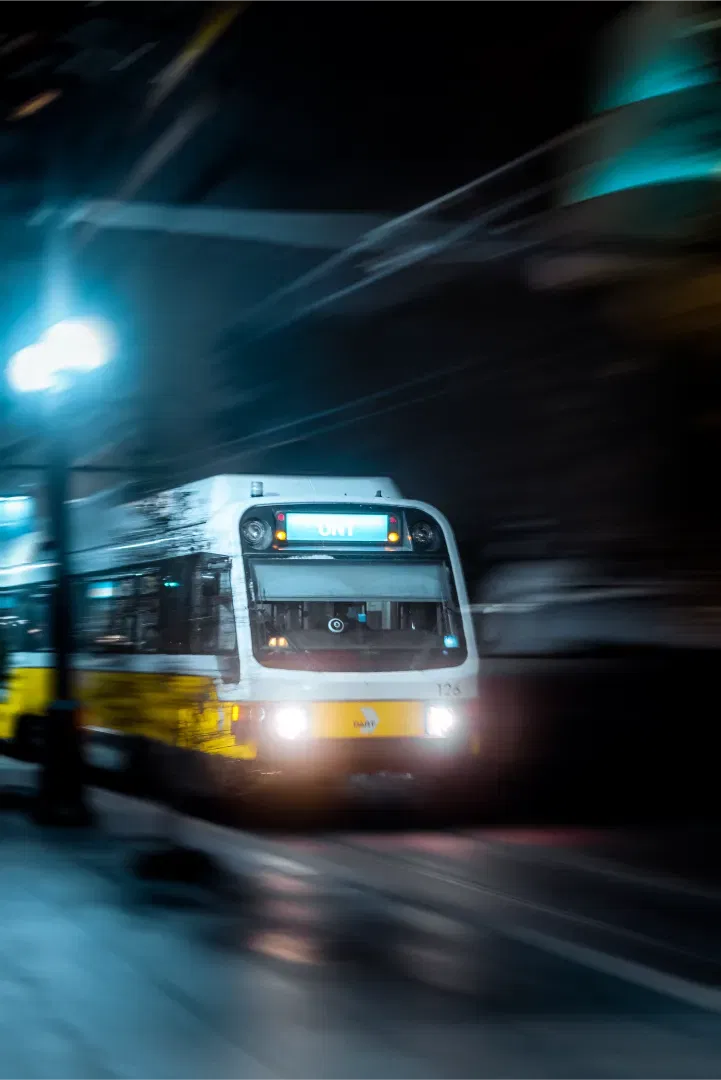 A fast-moving light rail train passing through a crossing at night, creating a dynamic motion blur.