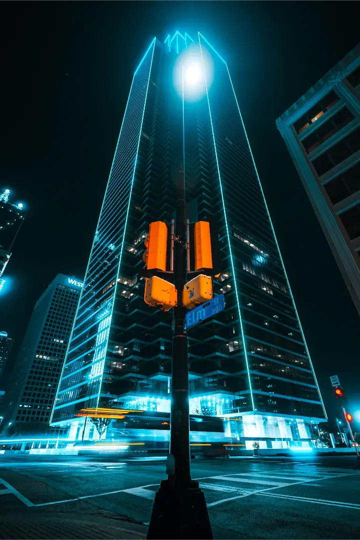 A wide angle shot of a neon-outlined skyscraper behind a traffic light structure at night.