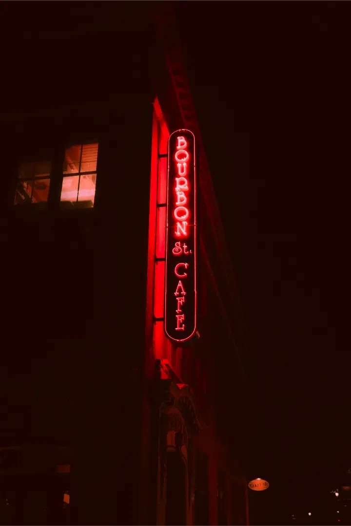 A vertical glowing red neon sign for Bourbon St. Cafe on a dark brick building facade at night.
