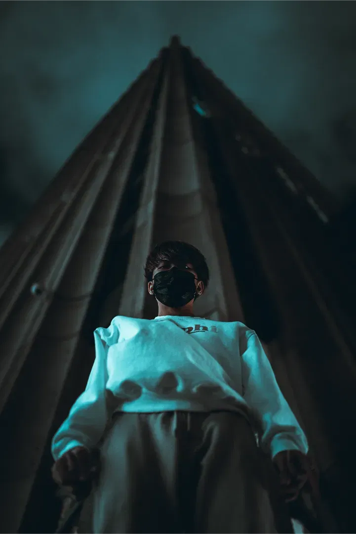Ultra low angle perspective shot of a person looking down at the camera, with a massive concrete building spire behind them.