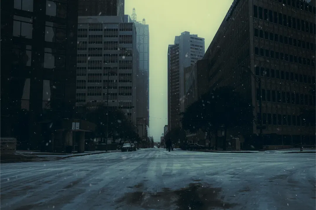 A desaturated, moody street scene in winter with tall buildings on both sides.