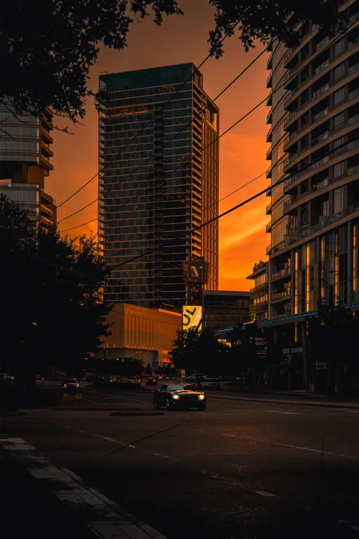City street scene at sunset, with a dramatic orange sky silhouetting a skyscraper in the center.