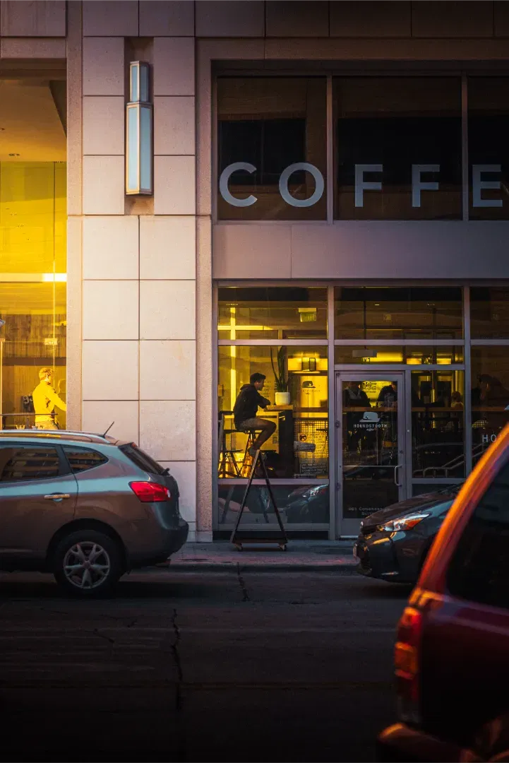 Street view of a modern COFFEE shop at night with warm interior lighting and cars parked outside.