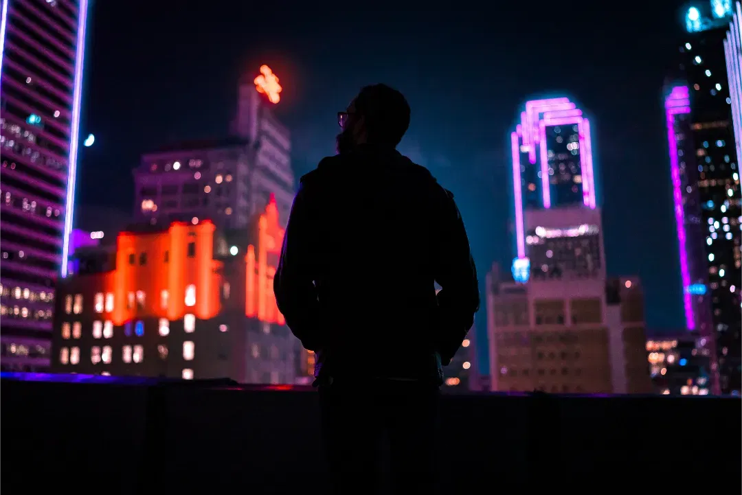 Silhouette of a man looking out at the colorful neon Dallas skyline at night, with pink and red lights.