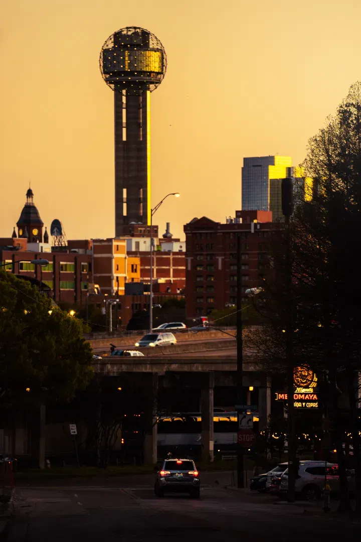 A view of Reunion Tower and the historic Dallas county courthouse at sunset with warm golden light.