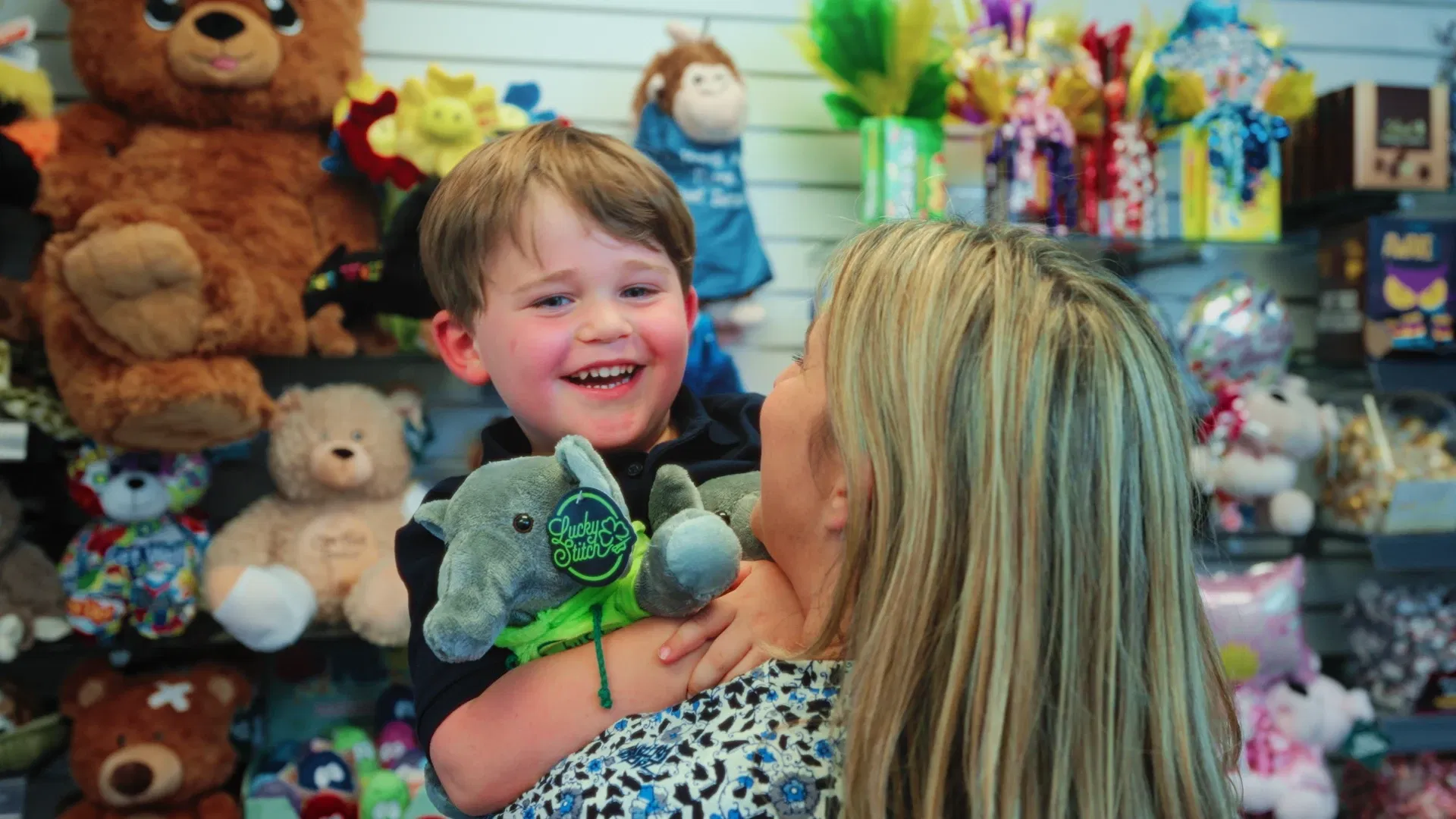 Smiling young boy and mother in a Cloverkey hospital gift shop holding a Lucky Stitch custom plush toy